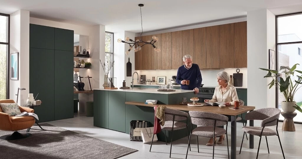 Ouder echtpaar pratend in een lange open keuken met een modern kookeiland en houten eettafel bij Meyer Totaal