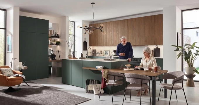 Ouder echtpaar pratend in een lange open keuken met een modern kookeiland en houten eettafel 